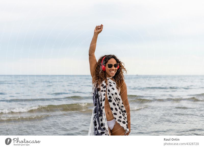 Glückliche junge schöne afroamerikanische Frau lächelnd, tragen Kopfhörer tanzen und heben Arm auf dem beach.Female genießen Sommerurlaub Konzept Lebensstil.