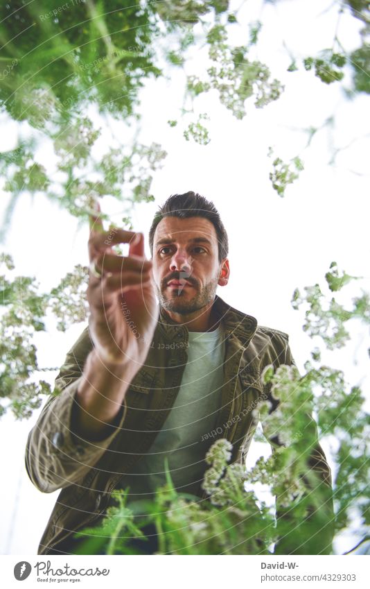 Mann betrachtet Blumen - unsere Umwelt Umweltschutz Pflanzen Klimawandel Garten Natur Naturphänomene betrachten untersuchen skeptisch Zukunftsangst