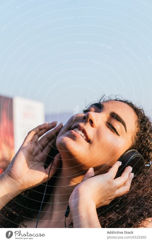 Junge Frau mit Kopfhörern genießt Musik auf der Straße zuhören Kälte sich[Akk] entspannen genießen sorgenfrei Glück Gesang jung ethnisch hispanisch krause Haare