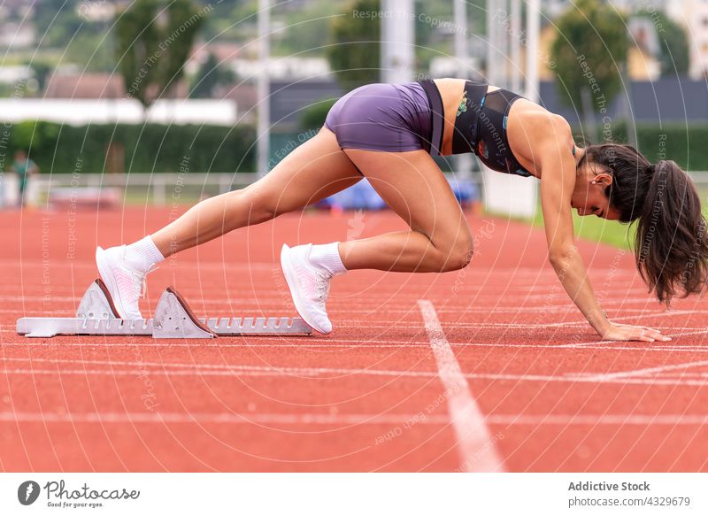 Leichtathletin bereit zum Sprint auf der Stadionbahn Sportlerin Athlet Sprinter Kauerstart Klotz Bahn Läufer Frau Start jung hispanisch Leichtathletik Training