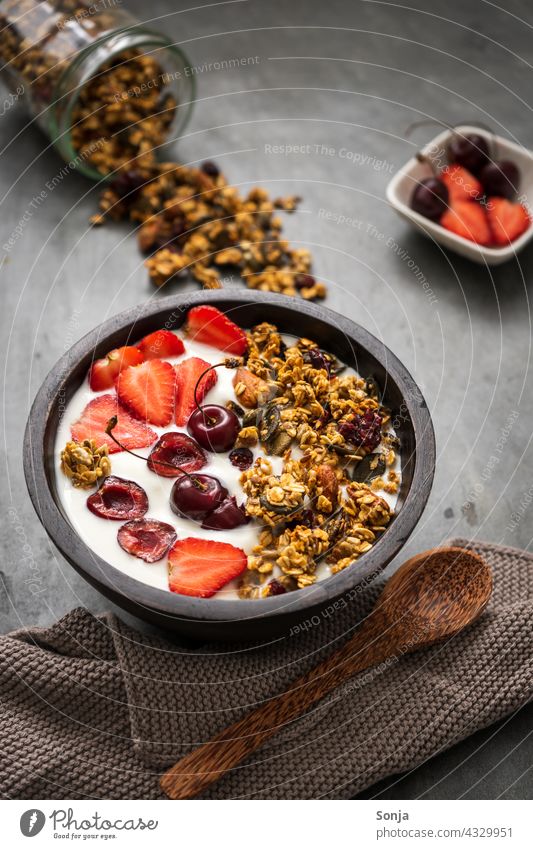Granola mit Joghurt und Erdbeeren in einer Schüssel auf einem rustikalen Tisch Frühstück Müslischale Morgen Löffel Holz Gesunde Ernährung Gesundheit Molkerei