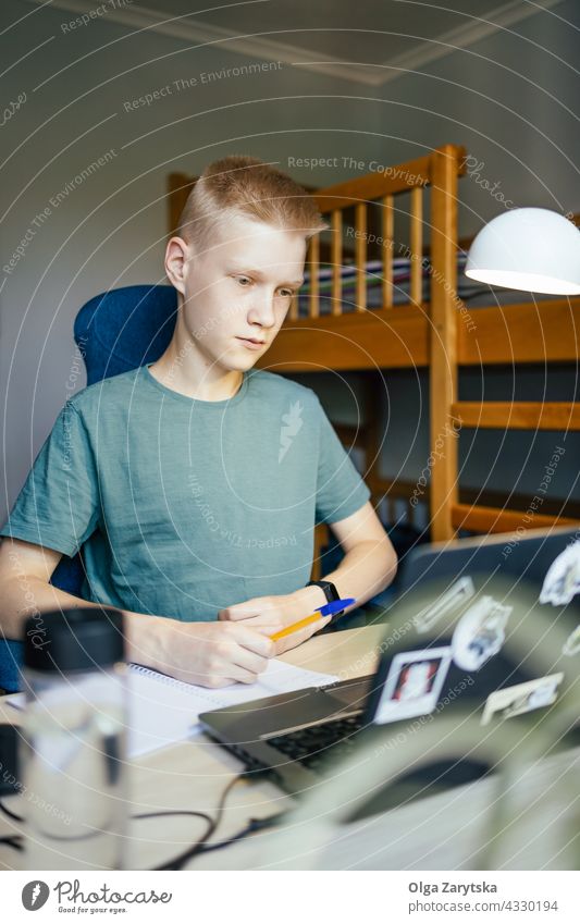 Junger Mann schreibt in ein Notizbuch. Schüler schreibend studierend online heimwärts Notebook arbeiten jung Schlafsaal Programmierer Bildung Hochschule Laptop