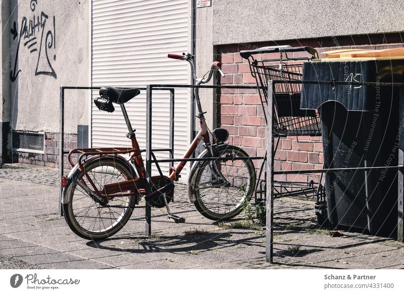 altes Klapprad am Fahrradständer Klappfahrrad Verkehrswende Stadtleben Einkaufswagen Mülltonne Rolladen Schatten