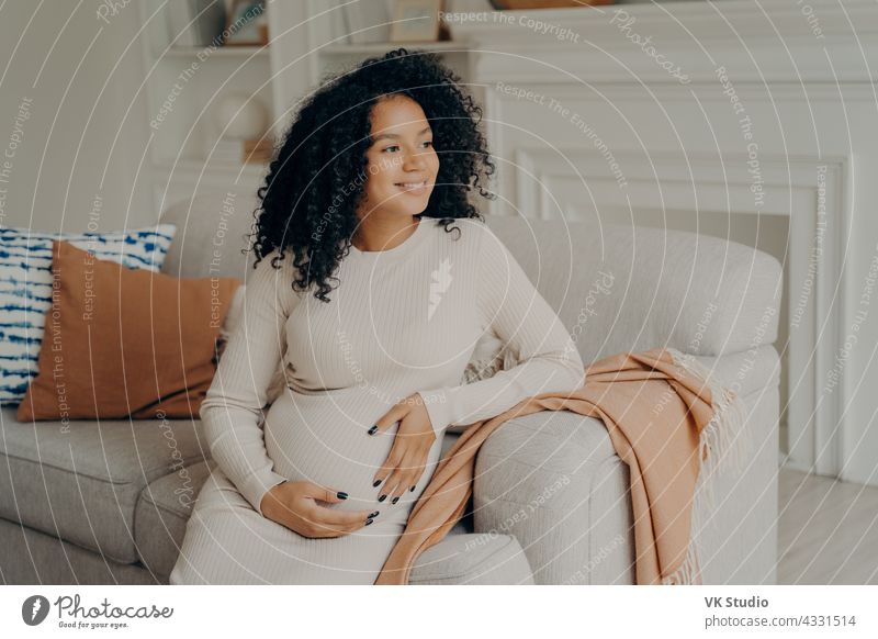 Schöne junge gemischte Rasse schwangere Frau umarmt ihren Bauch Sitzen Schwangerschaft Afrikanisch Sofa sich[Akk] entspannen ruhen Denken träumen Glück Baby
