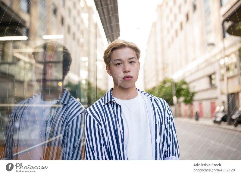Asiatischer Mann steht in der Nähe einer Glaswand in der Stadt Model Reflexion & Spiegelung Großstadt reflektieren Straße Stil selbstbewusst männlich ethnisch