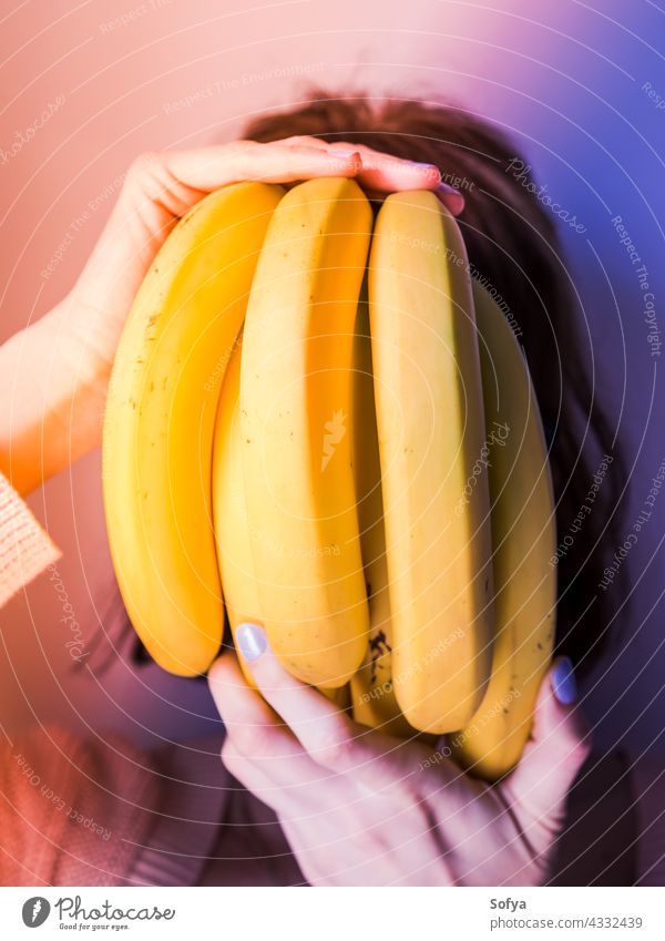 Frau, die ihr Gesicht mit einem Bündel Bananen bedeckt. Neon Kunst Haufen purpur Hand Maniküre neonfarbig Lebensmittel Design Konzept modern Trends Diät Mode