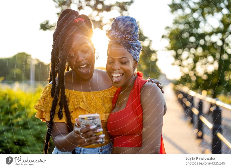 Zwei Freundinnen mit Smartphone, lächelnd im Freien Vielfalt Jahrtausende Zusammensein Freunde Freundschaft Schwesternschaft Schwarzes Leben ist wichtig