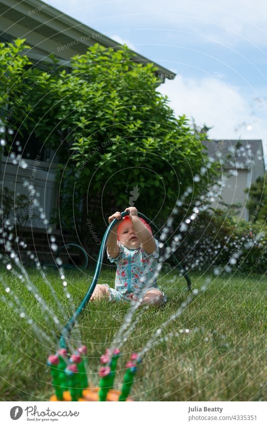 Junge Kleinkind halten auf Gartenschlauch beim Spielen in Sprinkler im Vorgarten Baby Sonnensicherheit Schlauch Sprinkleranlage Feinmotor ziehen Wasser