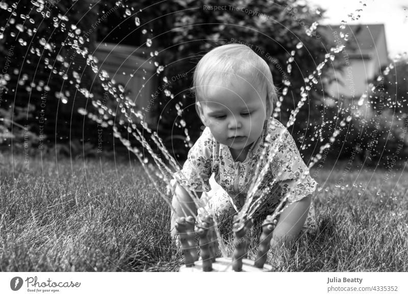 13 Monate altes Baby krabbelt zum Spielen auf einen Wassersprinkler Kleinkind Sonnensicherheit Sprinkleranlage Wasserspiel Hof heimwärts Viertel