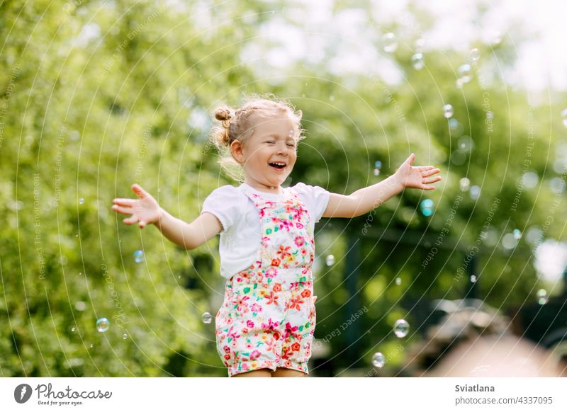 Ein fröhliches Mädchen fängt Seifenblasen mit ihren Händen und lacht. Glückliche Kindheit, Sommerzeit wenig Blasen Freude Baby grün Spaß Porträt Schlag schön