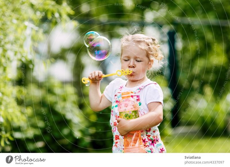 Ein kleines Mädchen bläst Seifenblasen im Park. Glückliche Kindheit, Sommerzeit. Seitenansicht wenig Blasen Freude Baby grün Spaß Porträt Schlag schön spielen