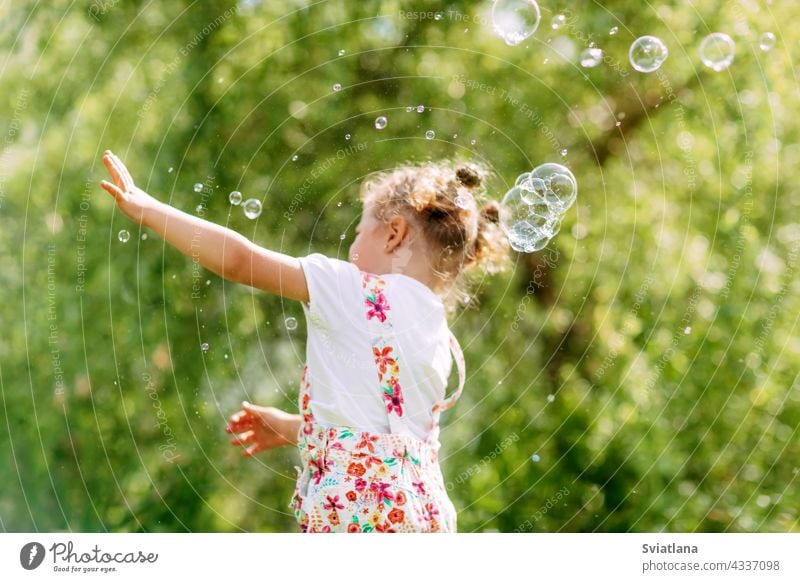 Ein fröhliches Mädchen fängt Seifenblasen mit ihren Händen. Fröhliche Kindheit, Sommerzeit. Seitenansicht wenig Blasen Freude Baby grün Spaß Porträt Schlag