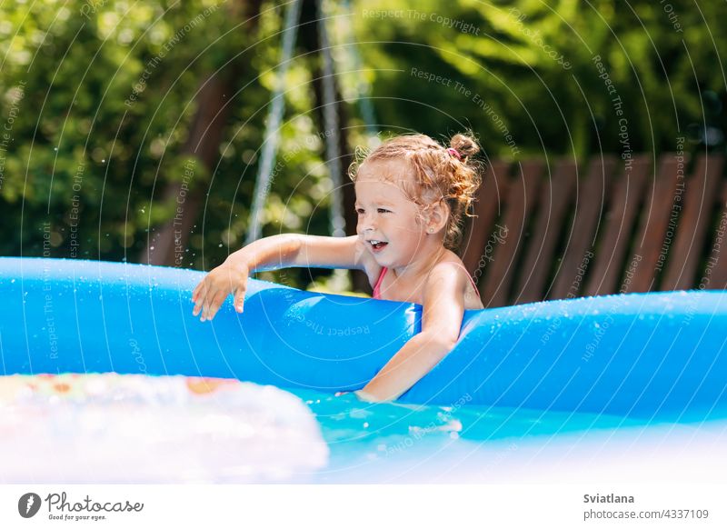 Ein charmantes Baby berührt das Wasser in einem aufblasbaren Pool im Garten und lächelt Mädchen Spielen Spaß Kindheit Sommer Schwimmsport Freude Badeanzug