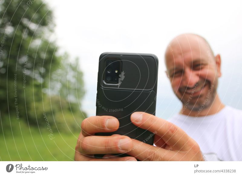 lächelnder Mann, der das Telefon in die Kamera zeigt, während er ein Foto macht Gefühle Toleranz Akzeptanz Frieden Solidarität lieblich multiethnisch