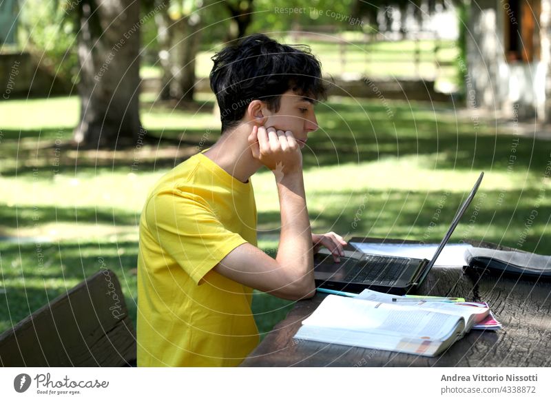 Männlicher Teenager, der draußen im Garten lernt, mit Platz für Ihren Text Junge Schüler Personal Computer Technik & Technologie Buch Lehrbuch Schönschreibheft