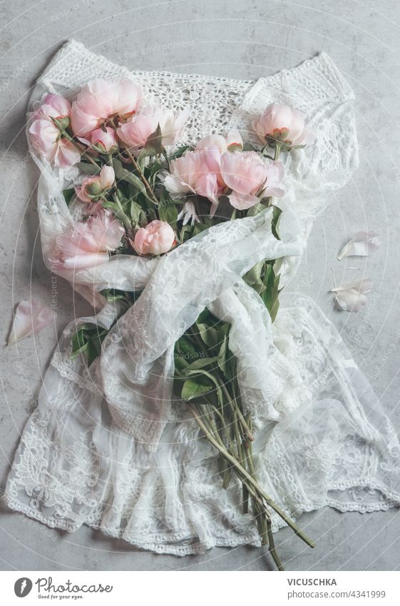 Schönes weißes Minikleid aus Spitze umarmt einen Strauß blassrosa Pfingstrosenblüten. Ansicht von oben schön Kleid Liebkosen Haufen Draufsicht breite Spitze