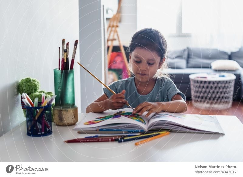 Kleines Mädchen malt zu Hause auf dem Tisch Farbe Glück spielerisch Frau Kinder spielen jung Fröhlichkeit Person Kunst Papier Inspiration wenig Bildung
