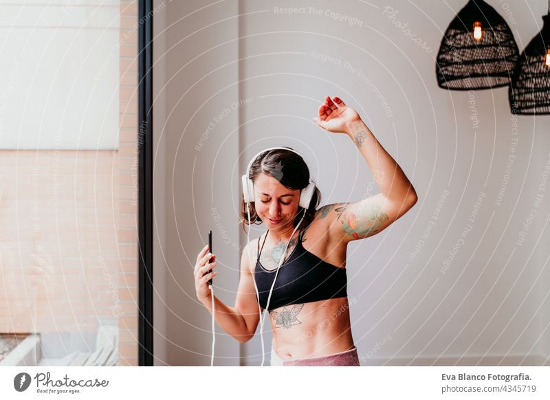 glückliche muskulöse kaukasische Frau, die Musik auf dem Handy und Headset in der Turnhalle hört. Tanzen am Fenster während der Tageszeit. Sport und gesunder Lebensstil