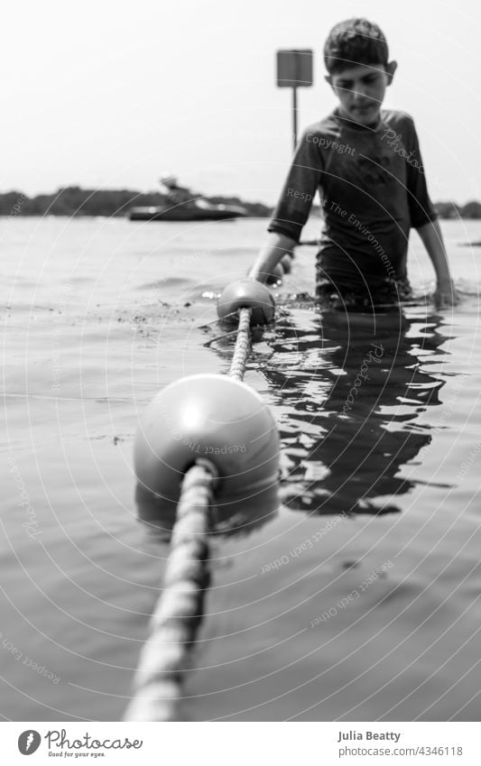Junge hält sich an einer Seilbarriere am See fest; Bojen am Seil waten Barriere Sicherheit vor dem Zehnten Autismus besondere Bedürfnisse vereinzelt