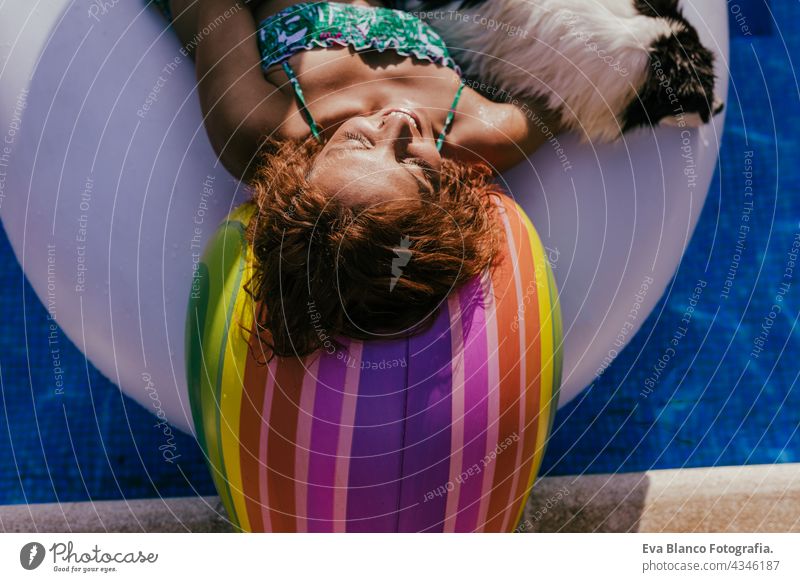 schöne kaukasische Frau sitzt auf aufblasbaren Einhorn Spielzeug im Schwimmbad. Netter Border Collie Hund daneben. Sommerzeit, Urlaub und Lebensstil fliegend