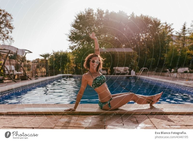 schöne kaukasische Frau sitzt am Pool Seite tragen Bikini-Badebekleidung. Sommerzeit, Urlaub und Lebensstil Kaukasier Schwimmbad Sonnenbrille heiß lustig sonnig