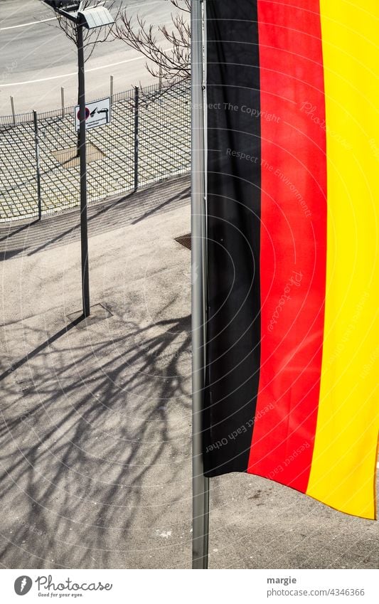 Blick von oben auf eine senkrechte Deutschland Flagge Fahne wehen Außenaufnahme flattern Menschenleer Fahnenmast Zaun Straßenbeleuchtung Schatten Farbfoto
