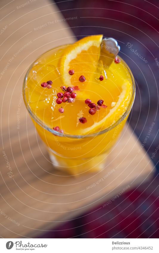 Nahaufnahme eines leckeren Getränks mit Kurkuma, Honig, Ingwer und Orange, gekrönt mit rosa Pfefferkörnern orange gelb trinken geschmackvoll Fotografie