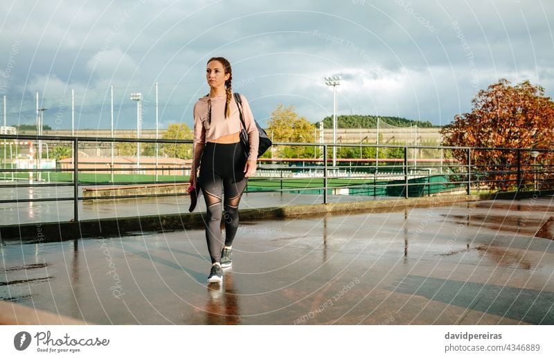 Sportlerin mit Sporttasche und Sportschuhen zu Fuß zum Training gehen Athlet laufen Turnschuh Textfreiraum nasser Boden regnerisch Morgen Fitness aktiv