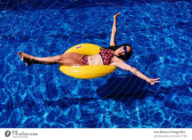 glückliche kaukasische Frau schwimmt auf gelben Donuts aufblasbare am Swimmingpool. Sommerzeit, Urlaub und Lebensstil Draufsicht Kaukasier fliegend Schwimmbad