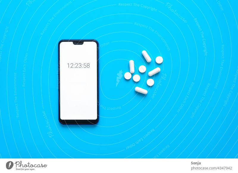 Smartphone mit Uhrzeit und weiße Tabletten auf einem blauen Hintergrund. Draufsicht. Erinnerung timer Bildschirm Telefon Gerät Blauer Hintergrund Alarm