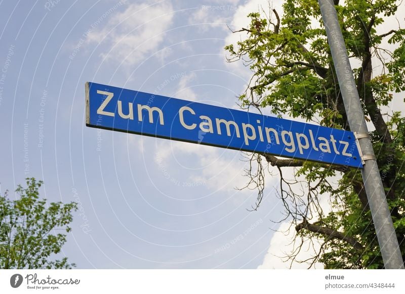 Straßennamenschild " Zum Campingplatz " an einer Eisenstange vor einem Baum / wohnen Schild Straßenschild Adresse Orientierung Schönwetterwolken Schrift
