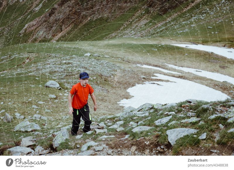 Kleiner Junge im roten T-Shirt vor einem Schneefeld auf einer Bergwiese mit Geröll in Südtirol Berge Wiese Wandern Steine wandern Berge u. Gebirge Landschaft