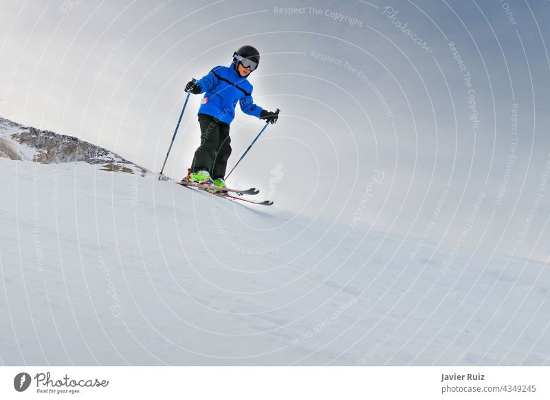 Kind mit Helm und blauer Jacke fährt schnell auf den Pisten Ski Skifahren Schutzhelm Winter Winterurlaubsort Skifahrer Schnee Kinder Lachen Laufwerk männlich