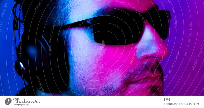 Neon-Porträt eines kaukasischen Mannes, der eine Sonnenbrille trägt und mit Kopfhörern Musik hört. Musik hören Person Atelier männlich Typ zuhören