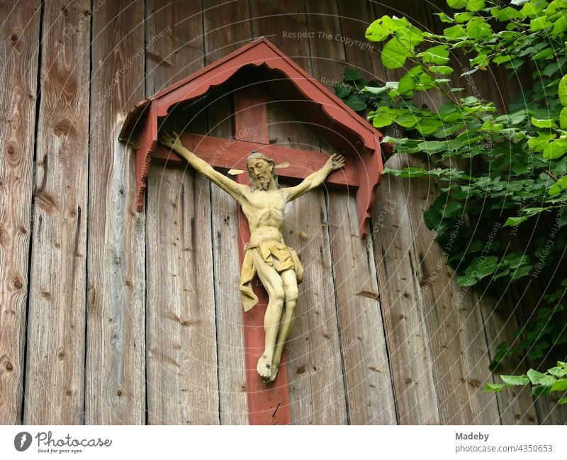 Kunstvolles Kruzifix mit Jesus Christus am überdachten Kreuz auf dem alten Holz einer Scheune in Rudersau bei Rottenbuch im Kreis Weilheim-Schongau in Oberbayern