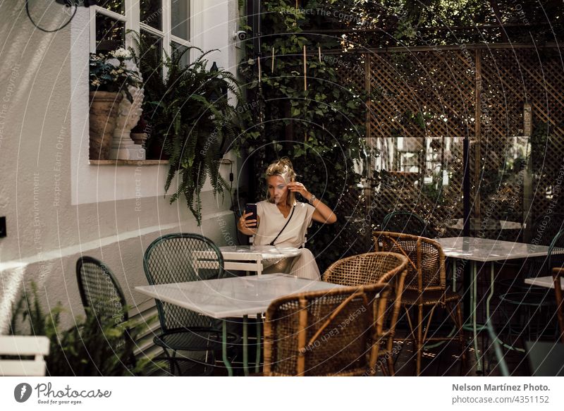 Blonde Frau nimmt ein Selfie auf der Terrasse eines Restaurants Komfortabel Lifestyle Porträt Smartphone selbstbewußt Tische vereinzelt allein blond Kaukasier