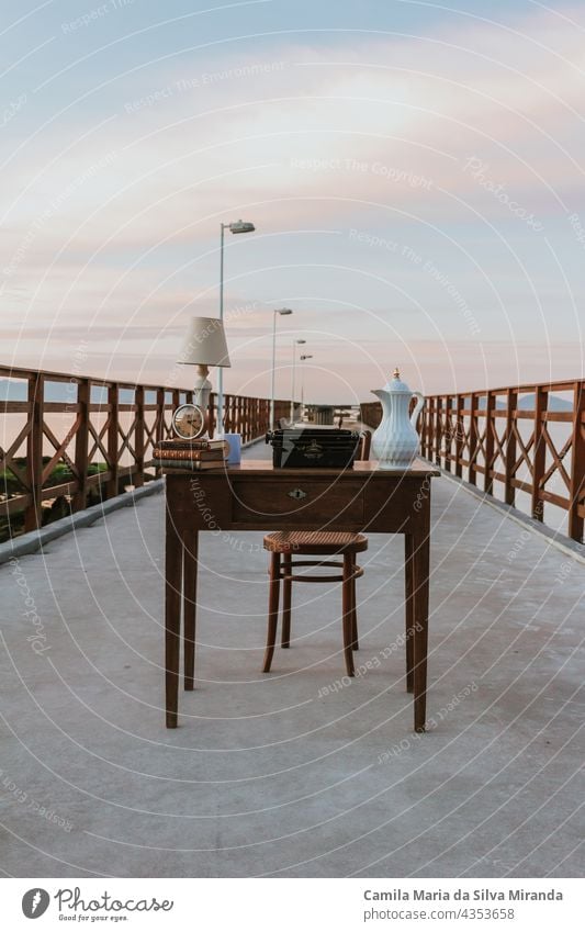 Alter Schreibtisch. Arbeitstisch auf einer Seebrücke. Arbeiten mit einer schönen Landschaft. Schreibtisch mit Büchern, Uhr, Lampe. Digitaler Nomade. Hintergrund