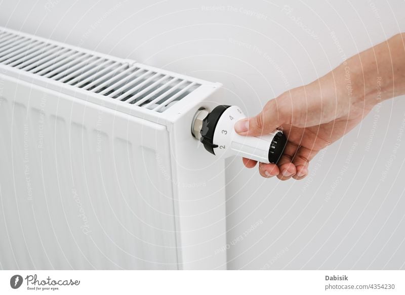 Frau stellt mit der Hand die Temperatur am Heizstrahler ein Heizkörper Thermostat erwärmen Knauf Ventil heimwärts Haus zentral Menschen kalt warm Energie Wand