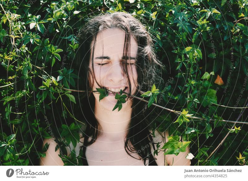 Seltsames Bild, auf dem ein junges Mädchen, umgeben von Pflanzen, in die Blätter beißt. lieblich brünett ungewöhnlich Auge langhaarig lustig im Freien Biss