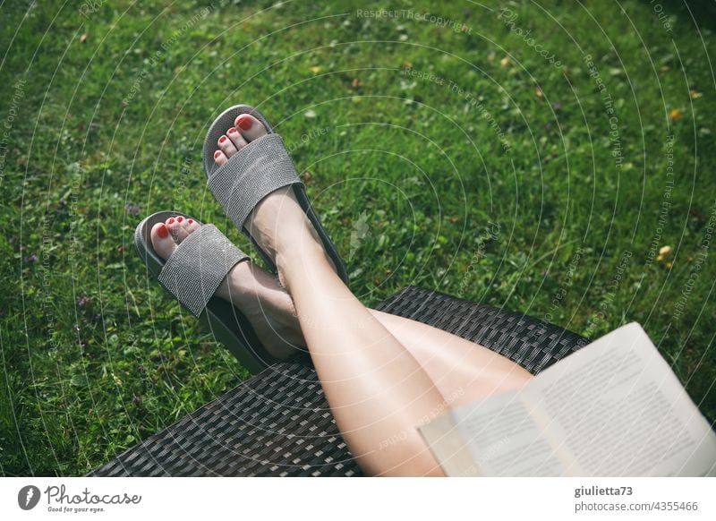 Nahaufnahme der weiblichen Füße in Glitzer-Badesandalen, entspannend im Garten, beim Buch lesen Beine Frau fuesse Damenschuhe Außenaufnahme Sommer Liege relaxen