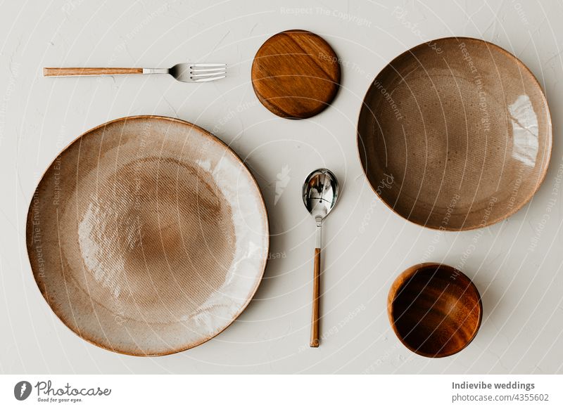 Zwei unterschiedlich große Teller mit einem Löffel und einer Gabel auf beigem Hintergrund. Flachlage, Ansicht von oben. Braune und naturfarbene Teller. Texturiertes körniges Muster auf den Tellern.