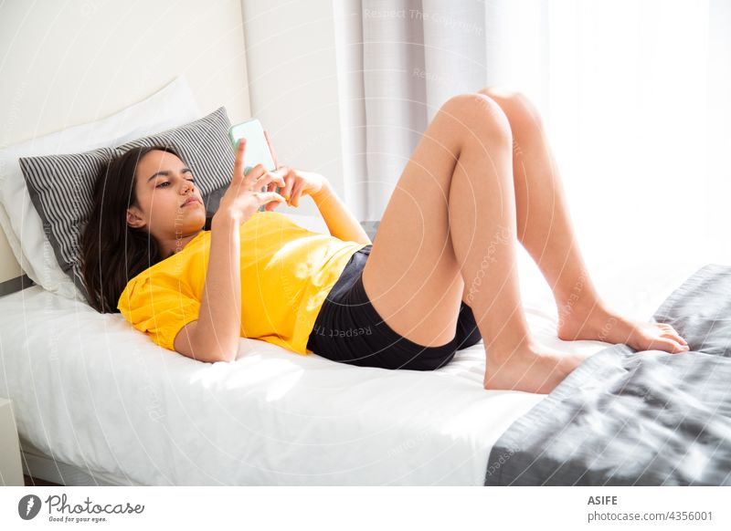 Konzentriertes Teenager-Mädchen, das im Bett liegend ihr Smartphone benutzt Technik & Technologie Mobile Telefon konzentriert fokussiert Schlafzimmer online