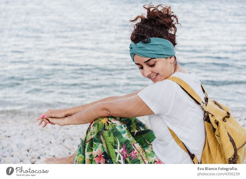 entspannte kaukasische Frau sitzt am Strand bei Sonnenuntergang. Wearing gelben Rucksack.Sommerzeit. daydreaming. Draußen Lebensstil Kaukasierin