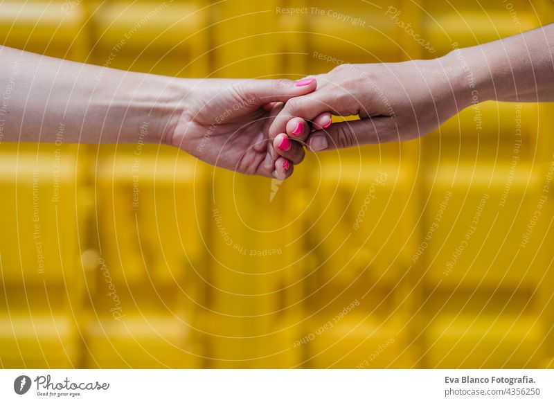 Nahaufnahme eines lesbischen Paares, das sich vor einem gelben Hintergrund an den Händen hält. Liebe ist Liebe. LGBTI-Konzept unkenntlich abschließen Glück