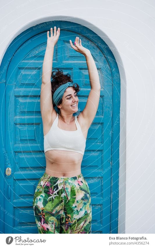 Porträt einer glücklichen kaukasischen Frau mit erhobenen Armen vor einer blauen Tür im Sommer. Lebensstil im Freien Glück Kaukasier blaue Tür Großstadt Strand