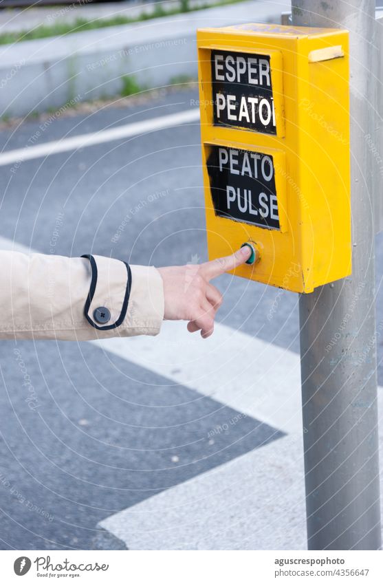 Der Finger einer Frau drückt auf die Fußgängertaste einer Ampel. Die Wörter, die erscheinen, bedeuten: "Fußgänger warten", "Fußgänger drücken". vertikal Presse