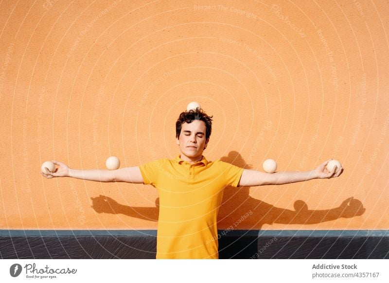 Ruhiger junger Mann mit Jonglierbällen an der Wand stehend jonglieren Ball Gleichgewicht unbeweglich ruhig Farbe Windstille bewegungslos Fähigkeit noch Trick