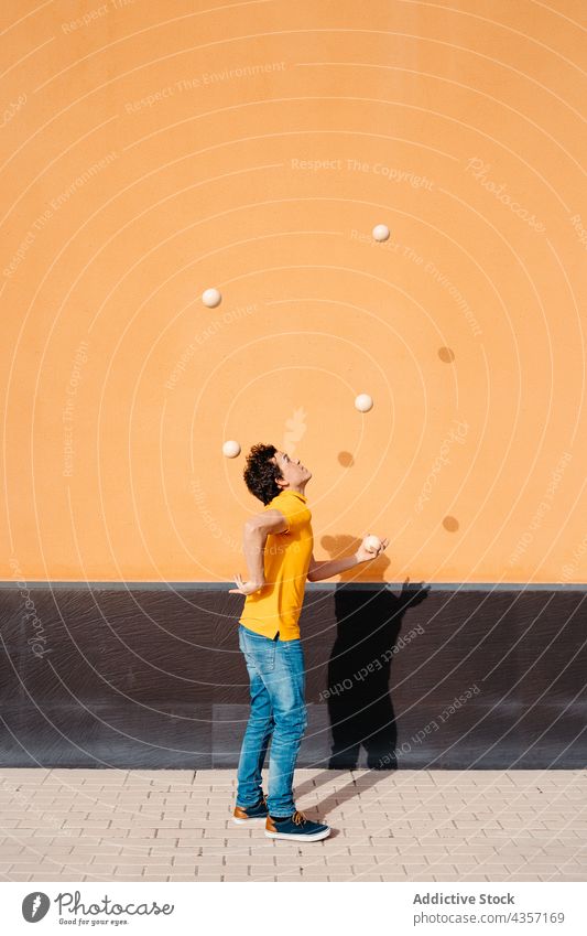 Agiler Mann jongliert Bälle in der Nähe einer bunten Wand jonglieren Trick Ball ausführen farbenfroh urban Talent Fähigkeit unterhalten männlich Kunst Aktivität