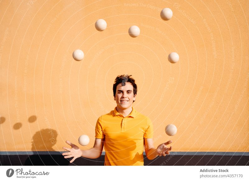 Agiler Mann jongliert Bälle in der Nähe einer bunten Wand jonglieren Trick Ball Lächeln ausführen farbenfroh urban Talent Fähigkeit Glück unterhalten männlich