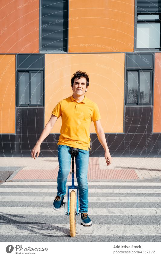 Junger Mann auf dem Einrad auf einer Stadtstraße Zebrastreifen Mitfahrgelegenheit urban Farbe modern orange Asphalt Straße Stil Gleichgewicht Rad männlich